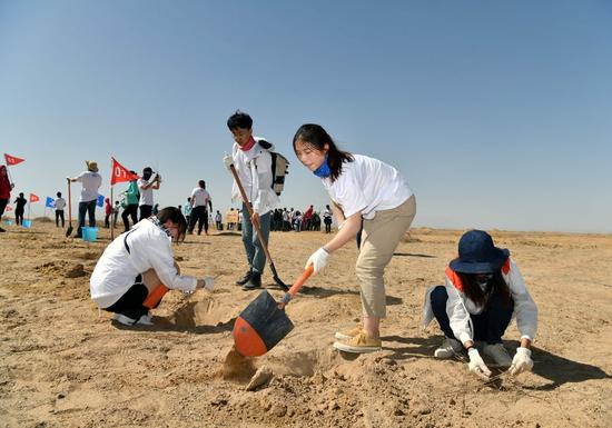 Volunteers plant trees sponsored by the Ant Forest initiative in a gobi desert in Dunhuang City, northwest China's Gansu Province on April 22, 2019. (Xinhua/Xu Kangping)