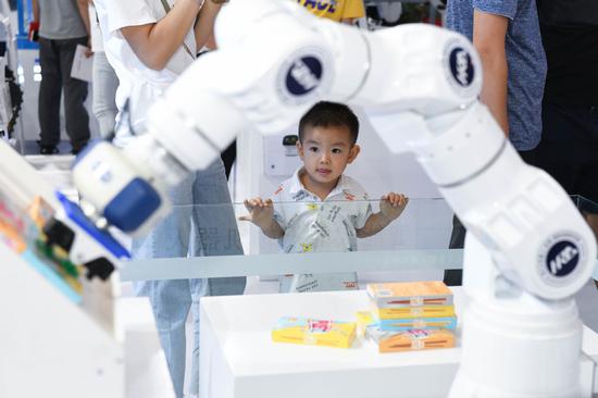 A young visitor looks at a robot during the world manufacturing convention in Hefei, capital of Anhui province. （Photo/Xinhua）