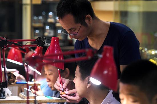 A craftsman (Up) teaches his apprentices fruit pit carving skills in Changsha, central China's Hunan Province, Sept. 18, 2019. (Xinhua/Chen Zeguo)