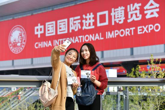 Visitors Chen Fei (L) and Weng Jingyi pose for photos in front of the venue of the first China International Import Expo (CIIE) in Shanghai, east China, Nov. 9, 2018. (Xinhua/Li Xin)