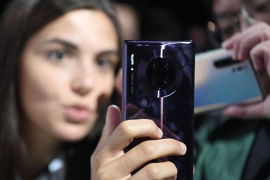 A Huawei's staff member (L) introduces a Mate 30 Pro smartphone to guests after a press conference hosted by Huawei in Munich, Germany, Sept. 19, 2019. (Xinhua/Lu Yang)