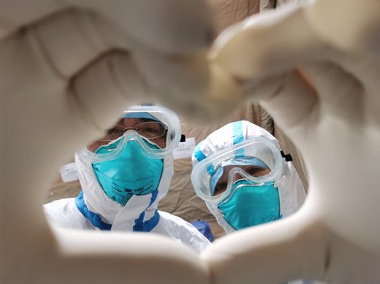 The couple Gao Yongzhe and Huang Wenli make a heart shape with their hands in Wuhan's Fang Cang makeshift hospital on Feb 14, 2020. (Photo by Gao Xiang/chinadaily.com.cn)