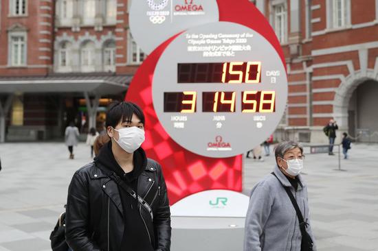 Pedestrians wearing face masks pass by an electronic countdown timer for the Olympic Games in Tokyo, Japan, Feb. 25, 2020. (Xinhua/Du Xiaoyi)