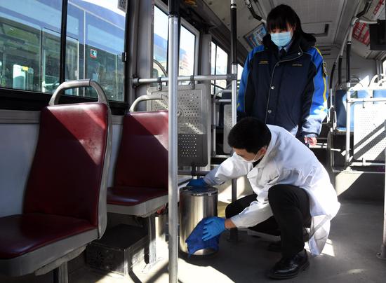Bus driver Li Tengfei (front) disinfects the garbage can on the bus in Beijing, capital of China, Feb. 16, 2020. (Xinhua/Ren Chao)