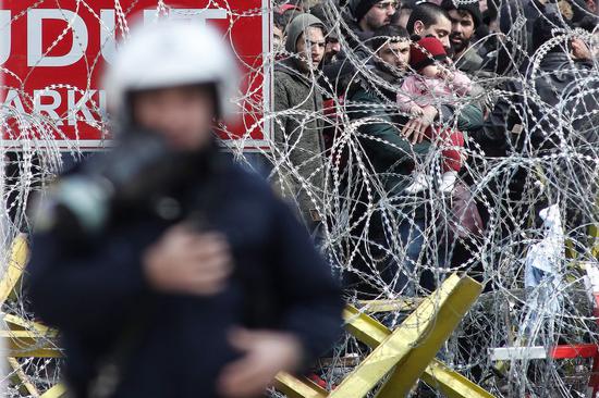 Migrants and refugees are seen behind a wired fence at the borderline between Greece and Turkey near the closed Kastanies border crossing in northeastern Greece, where thousands gathered near the Evros River in an attempt to cross into Greece, on March 2, 2020.(Photo by Dimitris Tosidis/Xinhua)