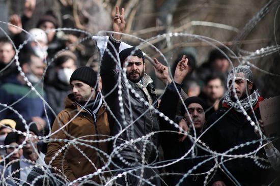 Migrants and refugees are seen behind a wired fence at the borderline between Greece and Turkey near the closed Kastanies border crossing in northeastern Greece, where thousands gathered near the Evros River in an attempt to cross into Greece, on March 2, 2020.(Photo by Dimitris Tosidis/Xinhua)