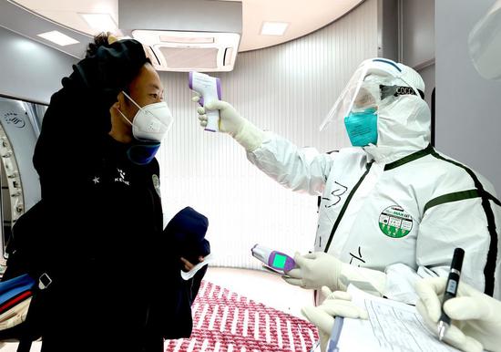 A customs officer measures the temperature of a passenger at the Beijing Capital International Airport in Beijing, capital of China, March 7, 2020. (Xinhua/Chen Jianli)