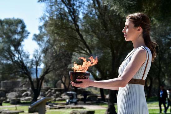 A performer is seen with the Olypmic Flame during the lighting ceremony in Ancient Olympia, Greece, on March 12, 2020. The Olympic Flame which will be burning for the Tokyo 2020 Olympics was ignited in Ancient Olympia in western Greece, the birthplace of the Games, on March 12, 2020. (Xinhua/Antonis Nikolopoulos)