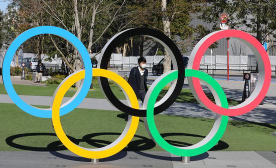 A pedestrian wearing mask walks past the Olympic rings in Tokyo, Japan, March 12, 2020. Japan's health ministry and local governments said Friday the number of COVID-19 infections rose by 21 to 697 cases in Japan as of 6:30 p.m. local time here. (Xinhua/Du Xiaoyi)