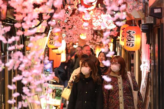 Pedestrians wearing masks walk under flowering cherry trees in Tokyo, Japan, March 5, 2020. (Xinhua/Du Xiaoyi)