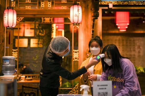 A customer registers as a staff member checks her body temperature at the entrance of a restaurant in Chengdu, southwest China's Sichuan Province, March 21, 2020. (Xinhua/Tang Wenhao)