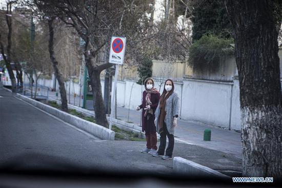 Women wearing masks are seen at an empty street in Tehran, Iran, on March 20, 2020.  (Photo by Ahmad Halabisaz/Xinhua)