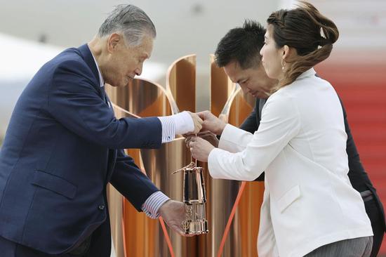 Olympic gold medalists Tadahiro Nomura (C) and Saori Yoshida (R) hand over the flame to President of Tokyo Organizing Committee of the Olympic and Paralympic Games (Tokyo 2020) Yoshiro Mori during the Olympic flame arrival ceremony in Miyagi of Japan, on March 20, 2020. (Kyodo News/Handout via Xinhua)