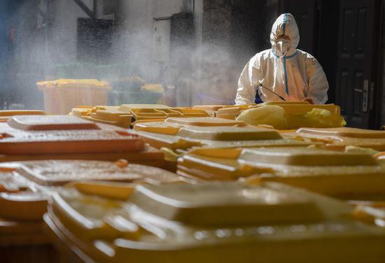 A worker of a company, which used to deal with industrial waste, disinfects disposal buckets filled with medical waste in Wuhan, central China's Hubei Province, March 5, 2020. (Xinhua)