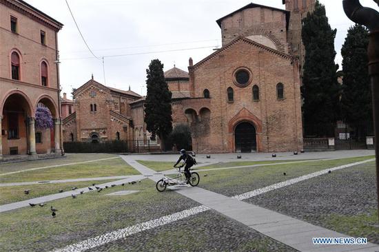 A person wearing a face mask rides a bicycle in Bologna, Italy, on March 30, 2020.   (Photo by Gianni Schicchi/Xinhua)