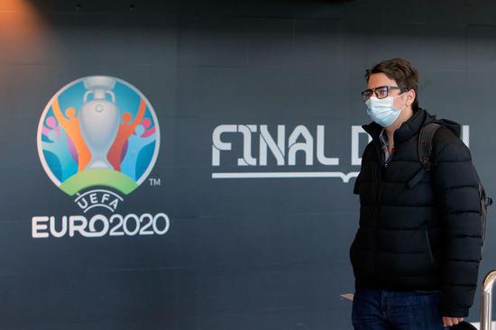 A man wearing a face mask passes by a logo of the EURO 2020 European Football Championship displayed on a wall at Henri Coanda International Airport in Bucharest, Romania, March 17, 2020. (Photo by Cristian Cristel/Xinhua)