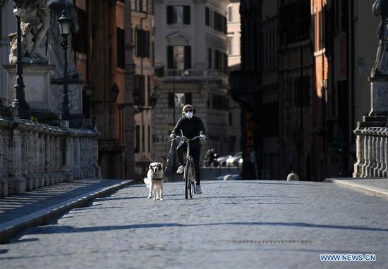 A woman wearing a face mask rides a bicycle and walks her dog in Rome, Italy, April 1, 2020. (Photo by Alberto Lingria/Xinhua)