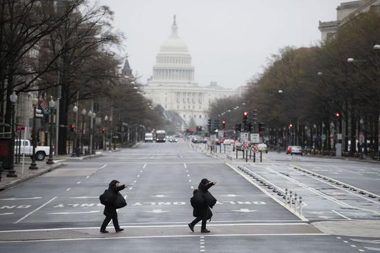 Photo taken on March 23, 2020 shows two pedestrians walking on a nearly empty street in Washington D.C., the United States. (Xinhua/Liu Jie)