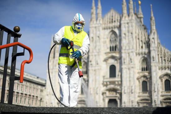 A sanitation worker wearing a protective suit and a face mask cleans the ground at Piazza del Duomo in Milan, Italy, on March 31, 2020. (Photo by Daniele Mascolo/Xinhua)