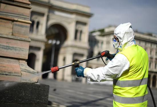 A sanitation worker wearing a protective suit and a face mask carries out the cleaning at Piazza del Duomo in Milan, Italy, on March 31, 2020. (Photo by Daniele Mascolo/Xinhua)