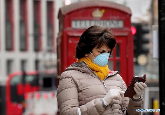 A woman wearing a mask waits for a bus on Shaftesbury Avenue in London, Britain, April 13, 2020. (Photo by Tim Ireland/Xinhua)