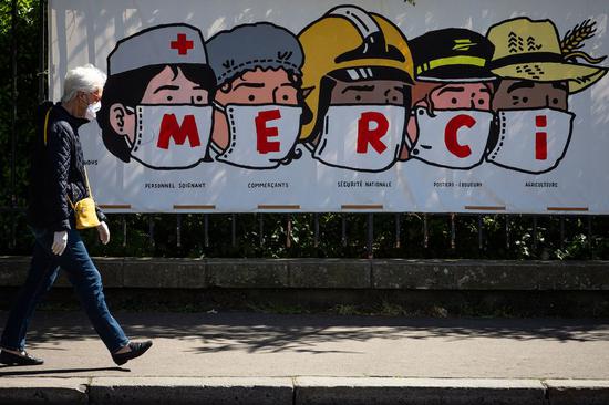 A resident walks past a poster thanking people in various professions during the epidemic in Paris, France, on April 14, 2020. (Photo by Aurelien Morissard/Xinhua)