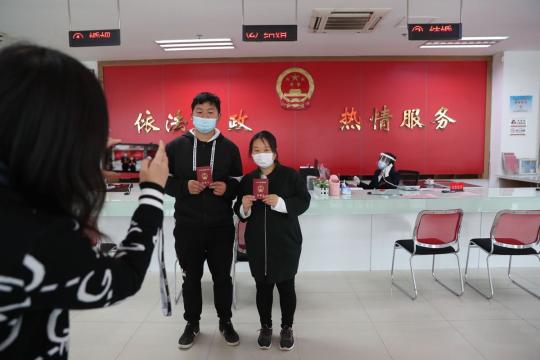 Xie Linhui (left) and Shang Qin get their marriage certificates at the marriage registration office in Qiaokou district in Wuhan, Hubei province, on Tuesday. (Photo by Wang Jing/China Daily)
