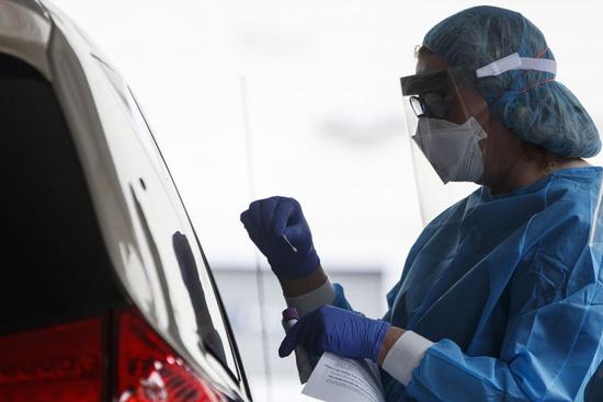 A medical worker at a COVID-19 drive-thru testing site uses a swab to take a sample at the George Washington University Hospital in Washington D.C., the United States, on April 9, 2020. (Photo by Ting Shen/Xinhua)
