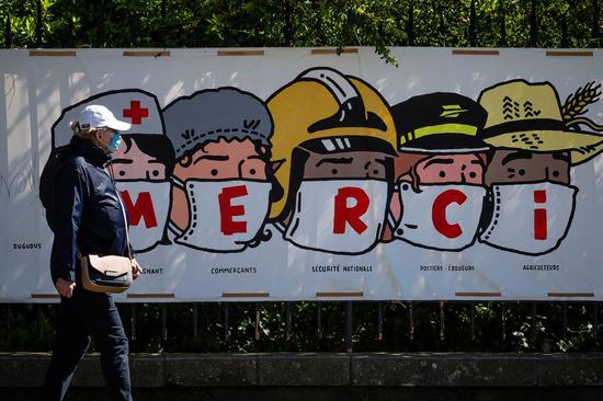 A resident walks past a poster thanking people in various professions during the epidemic in Paris, France, on April 14, 2020. (Photo by Aurelien Morissard/Xinhua)