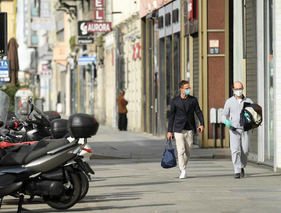 People wearing face masks walk on a street in Milan, Italy, on April 18, 2020. (Xinhua)