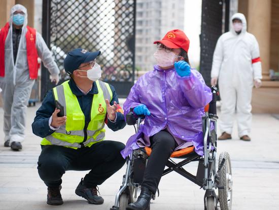 Du Chengcheng (in wheelchair) communicates with a volunteer as they deliver supplies to households at Jiangjiadun community in Wuhan, Hubei province, on March 1. (PHOTO/CHINA DAILY)