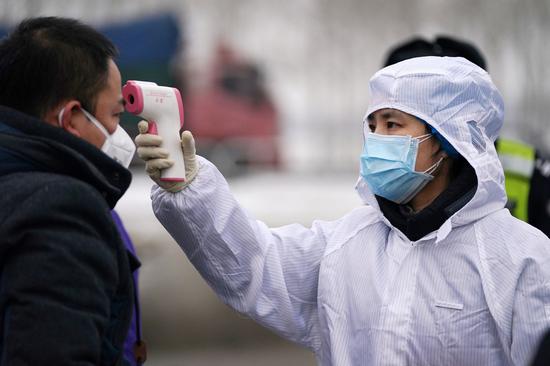 A staff worker takes a man's temperature at an expressway exit in Harbin, capital of Heilongjiang province, on Feb 21, 2020. (Photo/Xinhua)