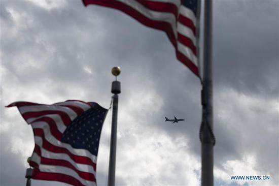 A plane flies in the sky with the U.S. national flags in the foreground in Washington D.C., the United States, on April 21, 2020. (Xinhua/Liu Jie)