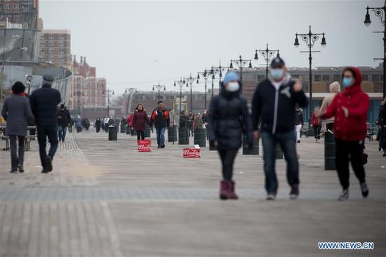 People walk on the Coney Island boardwalk in the Brooklyn borough of New York, the United States, April 19, 2020. (Photo by Michael Nagle/Xinhua)