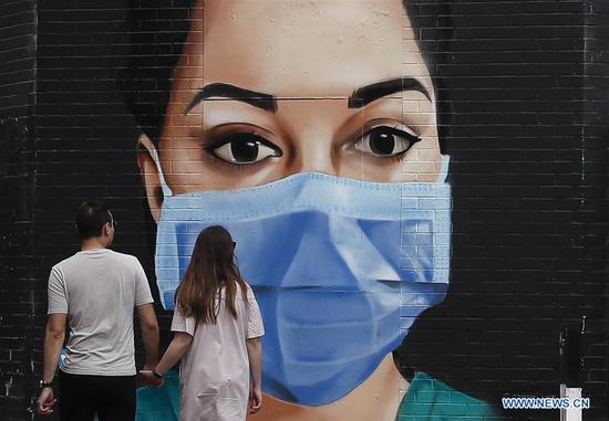 A couple walk hand in hand past a mural of a masked NHS (National Health Service) worker painted on a wall in London, Britain, on April 26, 2020. The number of confirmed COVID-19 cases in Britain hit 152,840 as of Sunday morning, marking a daily increase of 4,463, the Department of Health and Social Care said Sunday. As of Saturday afternoon, another 413 people who tested positive for the disease have died in hospitals, bringing the total number of coronavirus-related deaths in the country to 20,732, said the department. (Xinhua/Han Yan)