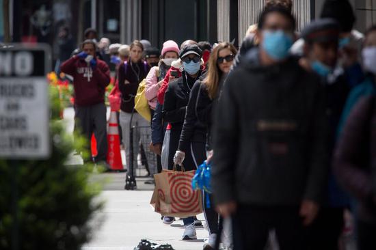 People wearing face masks wait in line to do shopping at a store during the coronavirus pandemic in the Brooklyn borough of New York, the United States, on April 14, 2020. (Photo by Michael Nagle/Xinhua)