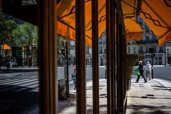 People wearing face masks walk past a closed restaurant in Paris, France, on April 26, 2020. (Photo by Aurelien Morissard/Xinhua)