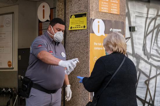 A security guard offers disinfectant gel to a woman at the entrance of a building in Barcelona, Spain, on May 11, 2020. (Photo by Sergi Camara/Xinhua)