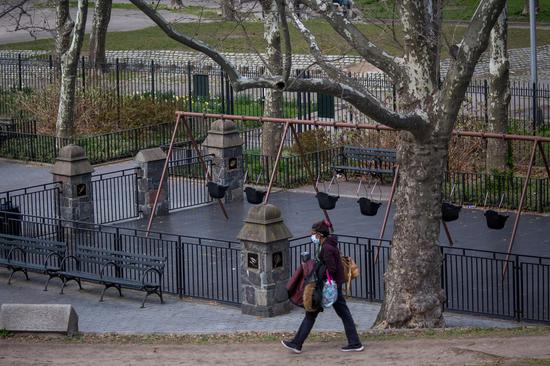 A woman wearing a face mask walks past a closed playground in Fort Greene Park in the Brooklyn borough of New York, the United States, April 2, 2020. (Photo by Michael Nagle/Xinhua)