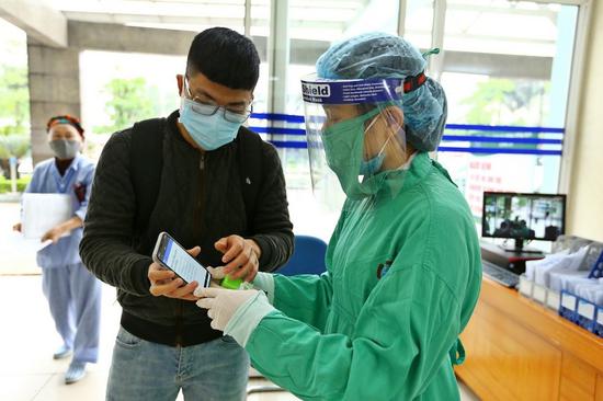 A medical worker instructs a man to register health condition online at a hospital in Hanoi, Vietnam, on April 7, 2020. (VNA/Handout via Xinhua)