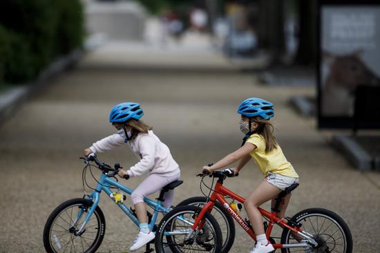 Children wearing masks ride bicycles on the National Mall in Washington D.C., the United States, May 18, 2020. (Photo by Ting Shen/Xinhua)