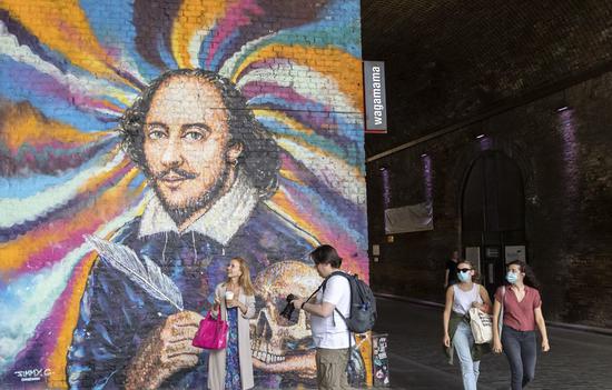 People wearing face masks walk by a mural in London, Britain, on Aug. 1, 2020. (Xinhua/Han Yan)