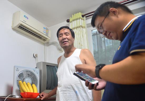Wang Hui (right) helps a blind senior set up smart appliances at the senior's home in Tianjin. （Photo provided to China Daily）