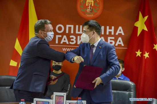 Chinese Ambassador to North Macedonia Zhang Zuo (R) touches elbow with mayor of Municipality Gazi Baba Borce Georgievski (L) during a signing ceremony of an agreement in Skopje, North Macedonia, Oct. 29, 2020. Chinese embassy in North Macedonia donates 310 tablets to school kids to help them have on-line classes. (Photo by Tomislav Georgiev/Xinhua)