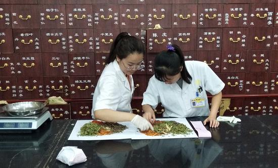 Photo taken with a mobile phone shows pharmacists preparing Chinese herbal medicine at a Chinese medicine store in Beijing, capital of China, July 31, 2019. (Xinhua/Zhang Chao)