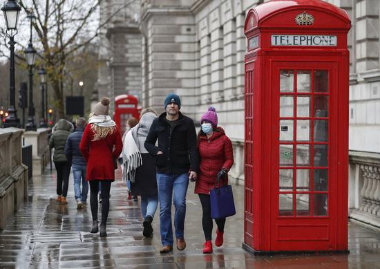 People wearing face masks walk past a red telephone box in central London, Britain, on Dec. 13, 2020. (Xinhua/Han Yan)