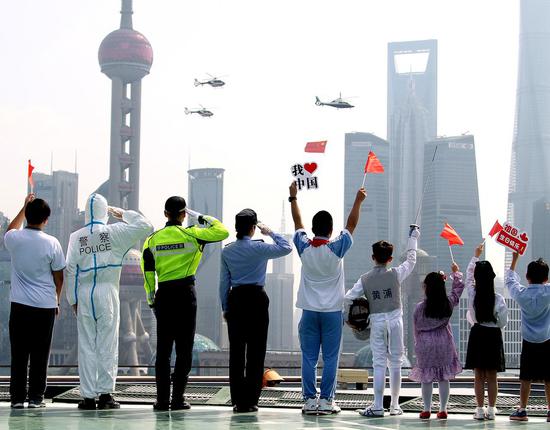 People salute as helicopters with Chinese national flag flies over the Huangpu River to celebrate the 71st anniversary of the founding of the People's Republic of China in Shanghai, east China, Oct. 1, 2020. (Xinhua/Chen Fei)