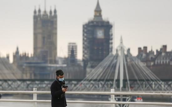 Photo taken on Dec. 29, 2020 shows a man walking along the Waterloo Bridge backdropped by the Houses of Parliament in London, Britain. (Xinhua/Han Yan)