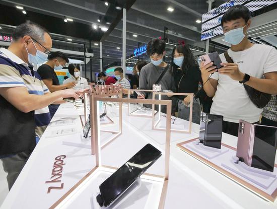 Visitors try Samsung Galaxy Z Flip 5G smartphones during a telecom expo in Guangzhou, Guangdong province, in November. (Photo by Li Zhihao/For China Daily)