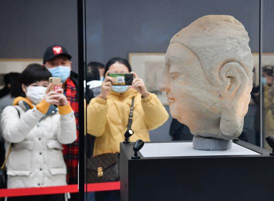 Visitors take photos of a stone Buddha head of a statue in Cave 8 of the Tianlongshan Grottoes during an exhibition at Luxun Museum in Beijing, capital of China, Feb. 12, 2021. (Xinhua/Li He)